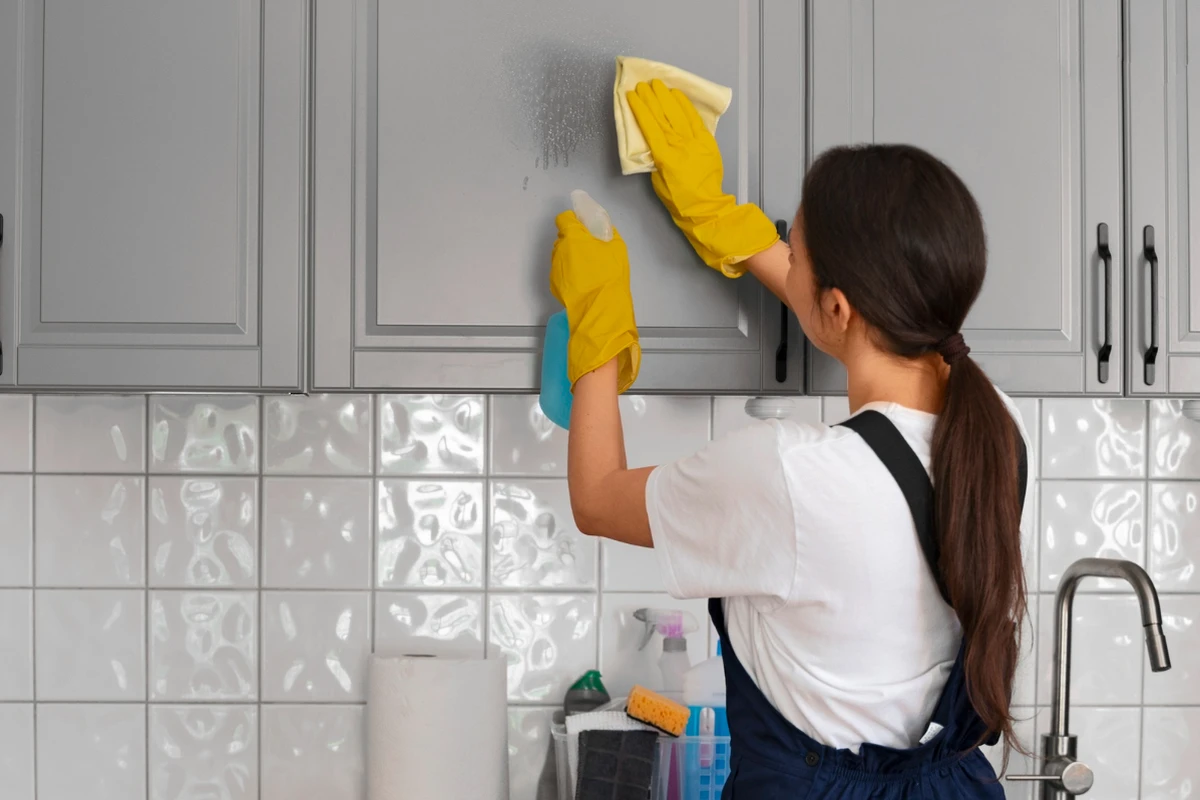 Cleaner wiping kitchen cabinet with yellow gloves and spray bottle